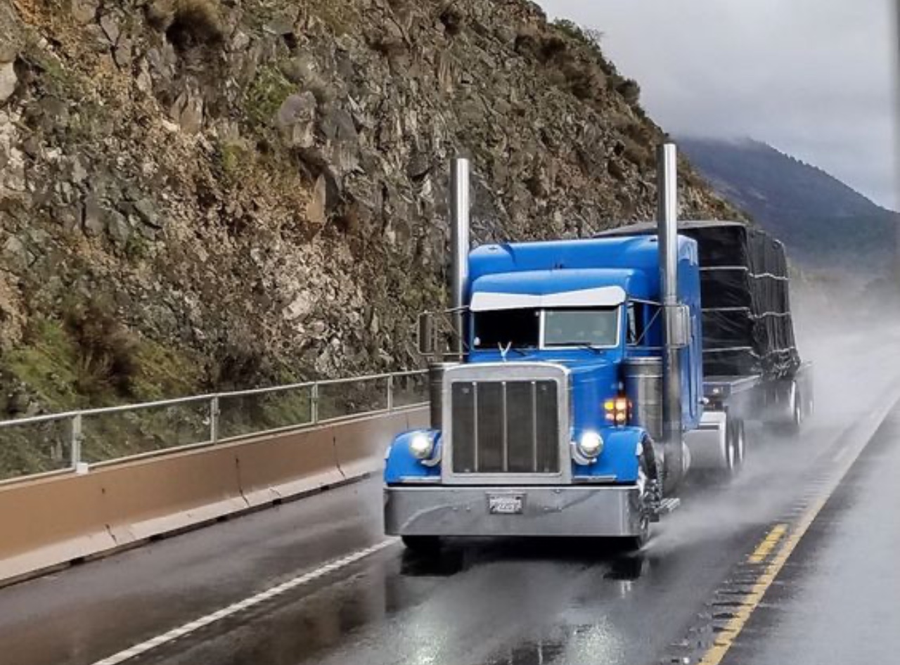 Semi Blue Tractor trailer truck on highway in the rain. Shippers-Freight Brokers